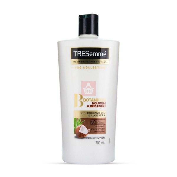 A 700ml bottle of Tresemmé Botanique Nourish & Replenish Conditioner. The bottle is white with a green flip-top cap, featuring the Tresemmé logo and product details. The label highlights key ingredients such as coconut milk and aloe vera, emphasizing its hydrating and replenishing benefits for dry and damaged hair. The packaging design conveys a natural and nourishing formula, suitable for daily hair care and moisture restoration.